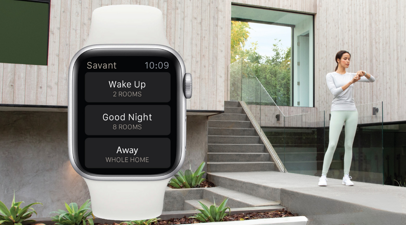 Woman standing outside her smart home, using a smart device to select automated scenes that enhance wellness through lighting, air quality, and comfort.